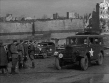 a black and white photo of a group of men standing around a military vehicle with a star on the side .