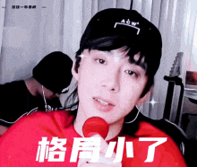 a young man wearing a black hat and a red shirt is holding a red microphone .