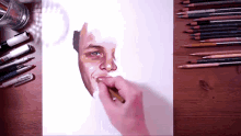a drawing of a man 's face is on a table with colored pencils and pens