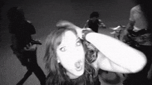 a black and white photo of a woman making a funny face in front of a group of people .