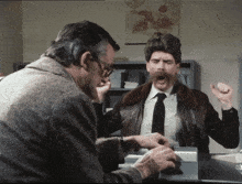 a man with a mustache is sitting at a desk with his mouth open