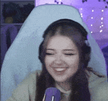a girl with purple hair is wearing headphones and smiling while sitting in a chair in front of a microphone .