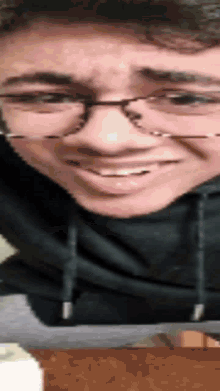 a man wearing glasses and a black hoodie smiles for the camera