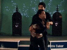 two men are dancing in front of a sign that says pisau ukur on it