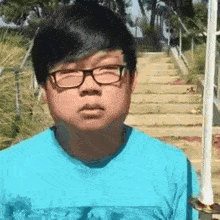 a young man wearing glasses and a blue shirt stands in front of stairs .