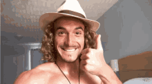 a shirtless man wearing a hat gives a thumbs up sign