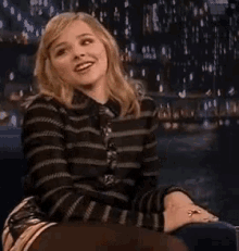 a woman in a striped sweater and tie is sitting in a chair .
