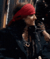 a woman wearing a red headband and a black jacket is standing in front of a building .