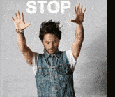 a man in a denim vest has his hands in the air and the word stop is above him