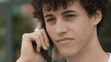 a young man with curly hair is talking on his cell phone