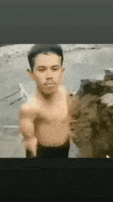 a shirtless man is standing next to a rock in the water .