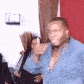 a man in a blue shirt is dancing in a room with a woman behind him .