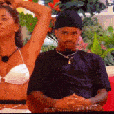 a man in a black hat sits next to a woman in a white bikini