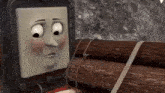 a cartoon train is standing next to a pile of logs and looking at the camera .