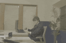 a man in a suit sits at a desk talking on a phone