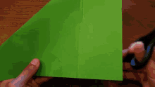 a person is cutting a piece of green paper with a pair of scissors .