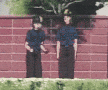 two police officers standing next to each other in front of a brick wall .