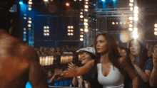 a woman in a white tank top stands in front of a crowd at a concert