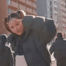 a woman in a ponytail is standing in front of a building and smiling .