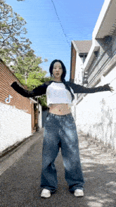 a woman wearing a crop top and wide leg jeans is standing on a street .