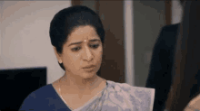 a woman in a blue shirt and a pink saree is looking at the camera .