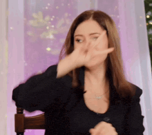 a woman in a black jacket is sitting in a chair covering her face with her hand .