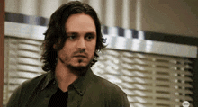 a man with long hair and a beard is standing in front of a abc sign