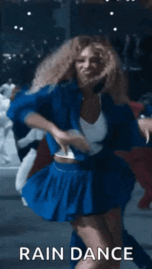 a woman in a blue skirt is dancing in front of a crowd in a rain dance .