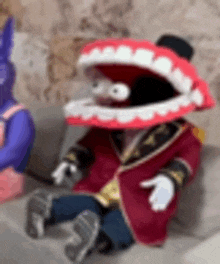 a stuffed animal with a large mouth is sitting on a couch next to another stuffed animal .