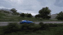 a blue car is driving down a road with trees on the side