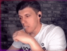 a man in a white t-shirt is smoking a cigarette while wearing ear buds .