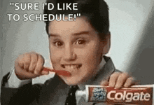 a young boy is brushing his teeth with a toothbrush and a tube of colgate toothpaste .