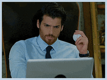 a man in a blue shirt and tie is sitting in front of a laptop computer holding a baseball ..