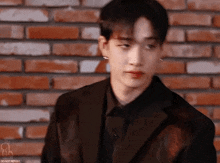 a young man in a suit is standing in front of a brick wall and looking at the camera .