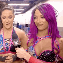 a woman with purple hair is holding a microphone and talking to another woman .