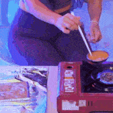 a person is cooking on a red stove that says ' portable ' on the side