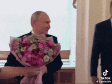 a man in a suit is being presented with a bouquet of pink flowers