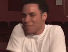 a man in a white shirt is smiling with his eyes closed in a dark room