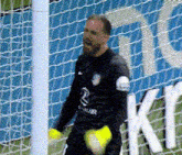 a soccer goalie is holding a ball in front of a net with the letter k on it