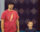 a man wearing a red shirt with a lightning bolt on it stands next to a young boy