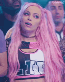 a woman with pink hair and a choker is making a funny face while standing in front of a crowd .