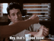 a man sits at a table with a cup of coffee and says " hey that 's a good book "