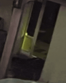 a person is standing in a dark room with a yellow light coming out of a door .