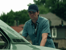 a man wearing a baseball cap and a blue shirt stands next to a car