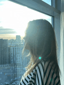 a woman in a striped shirt looks out a window at a city