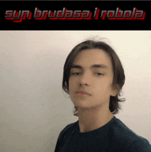 a young man stands in front of a sign that says syn brudasa i robota
