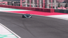 a race car is driving down a track with a red barrier behind it