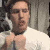 a man in a white shirt is adjusting his tie and making a funny face