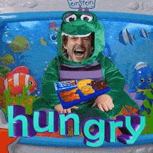 a child in a frog costume is holding a tray of food and the word hungry is visible