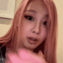 a woman with pink hair is holding a pink object in her hand and looking at the camera .